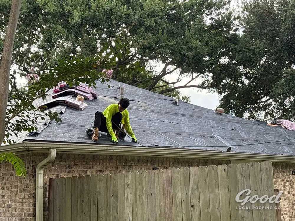 Roofer removing old shingles, exposed decking visible along the slope.