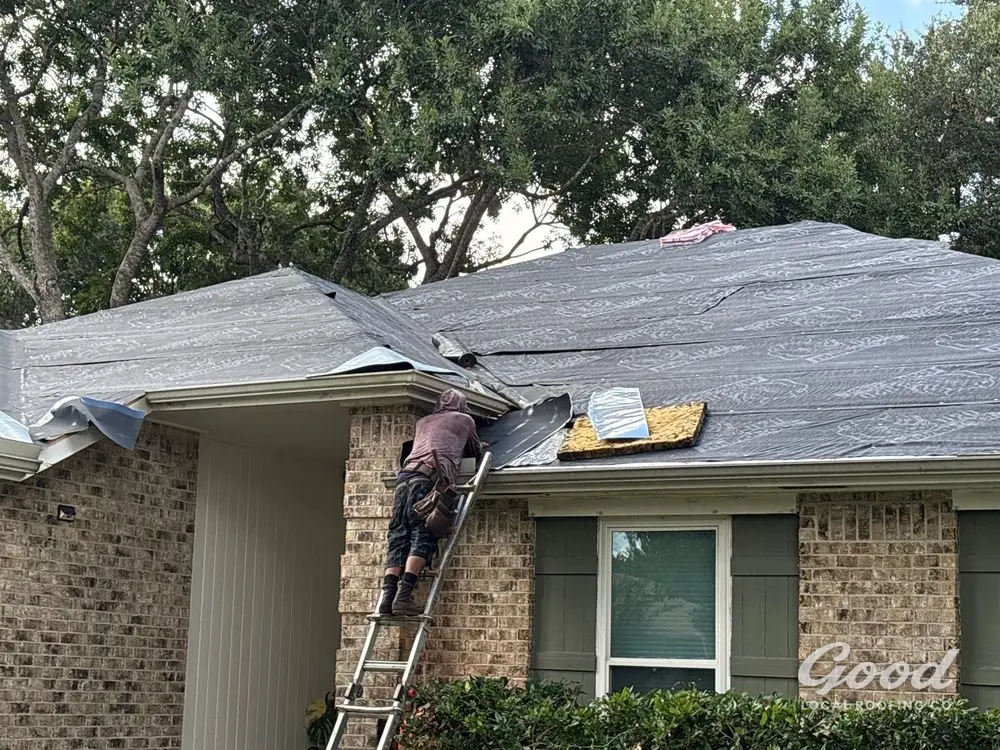 Roofer on a ladder at the eave fitting underlayment and eave protection.